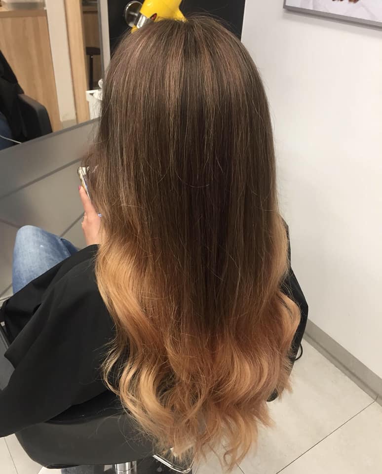 Długie, brązowe włosy z koloryzacją ombre w ciepłym, jasnym odcieniu karmelu/blondu na końcach. Włosy falowane, praca Salonu Agneess.