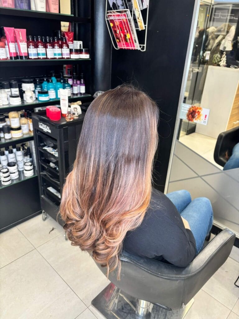 Klientka w fotelu po koloryzacji Sombre – lśniące włosy, odbicie lustrzane i widoczne produkty L'Oréal i Kérastase w tle salonu Agneess.