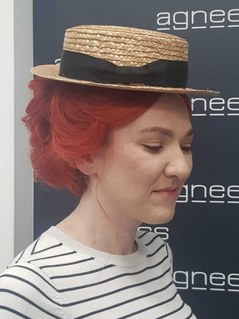 Fryzura inspirowana epoką – czerwone upięcie z kapeluszem, widok z boku